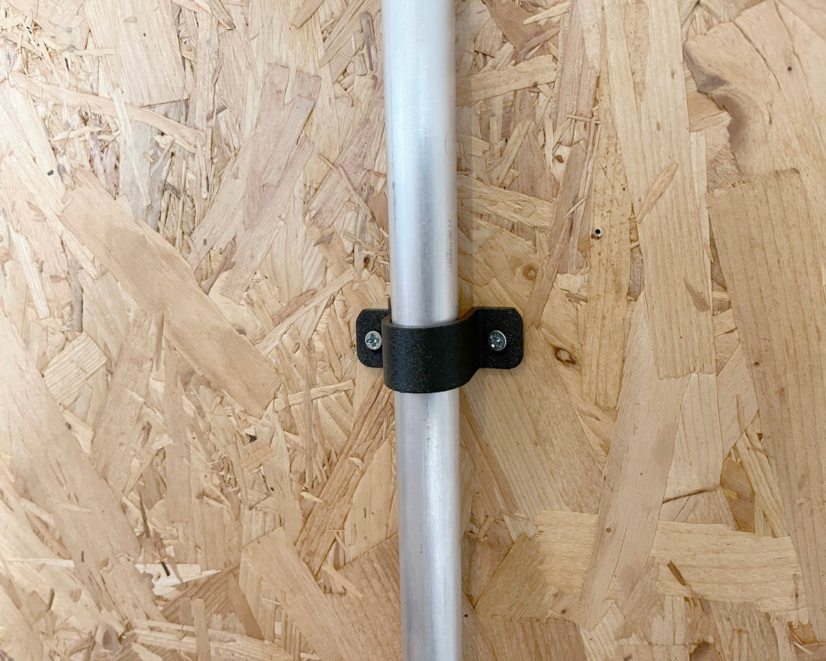 A silver metal pole secured with a black plastic and metal mounting bracket against an OSB wood panel background.