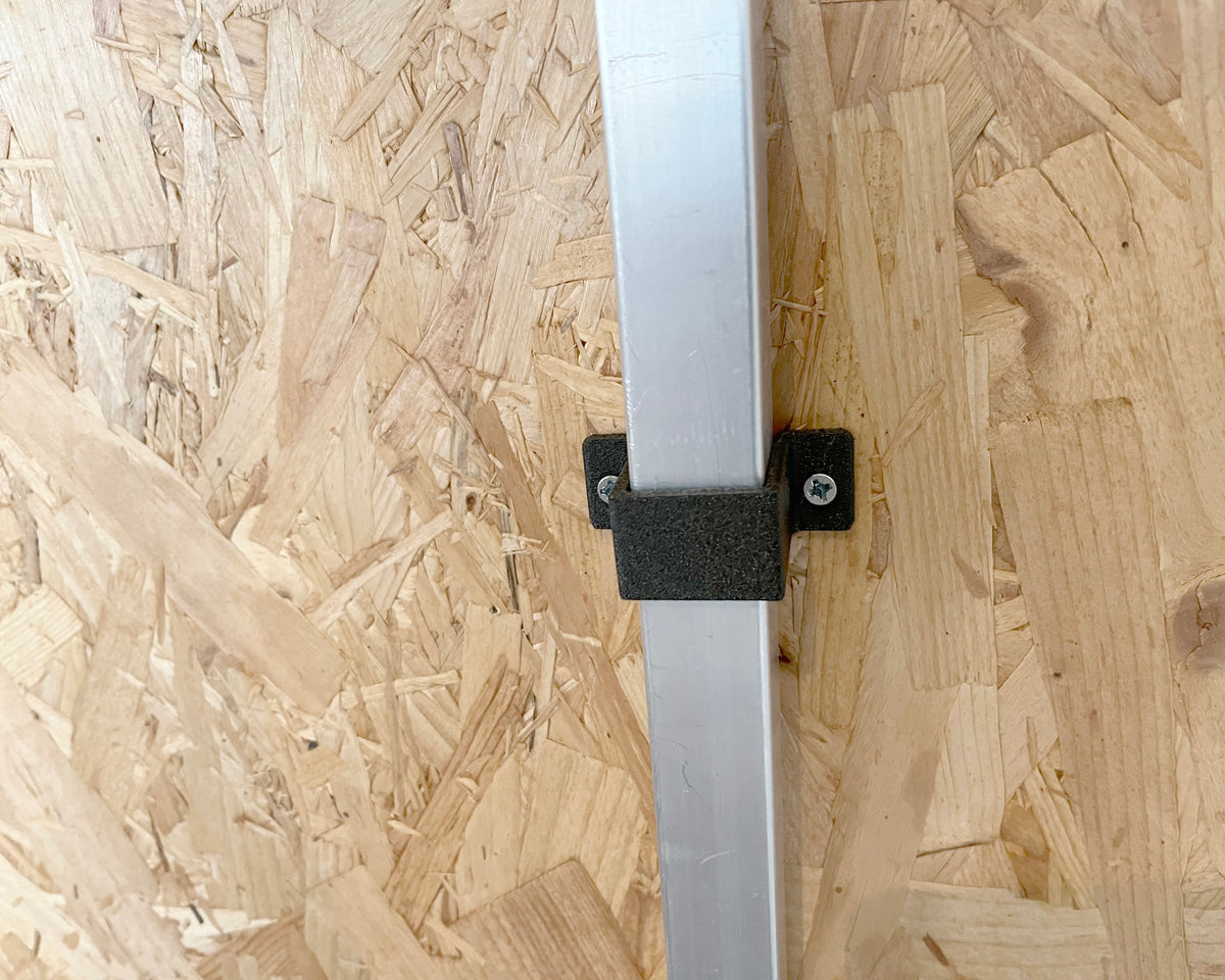 A close-up of a silver metal vertical post secured with a black mounting bracket against an OSB wood panel background.